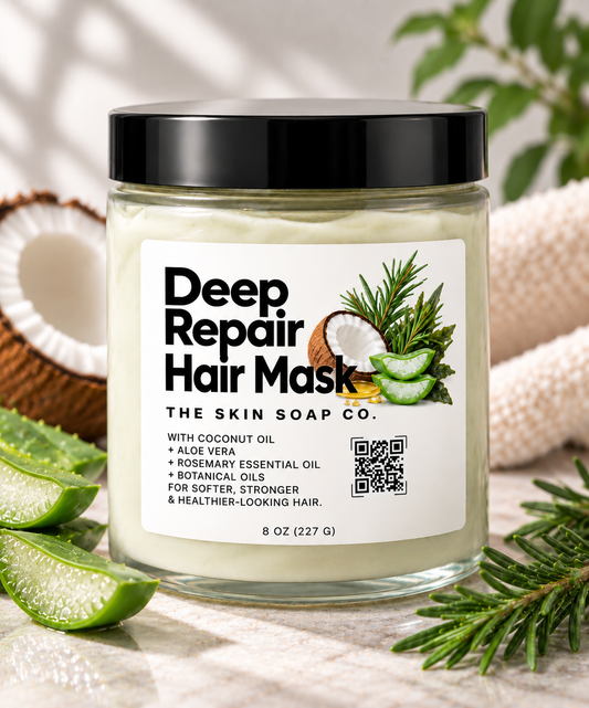 A jar of Deep Repair Hair Mask by The Skin Soap Co. with coconut oil, aloe vera, rosemary, and botanical oils, styled with aloe slices, a coconut half, and pine needles on a marble surface.